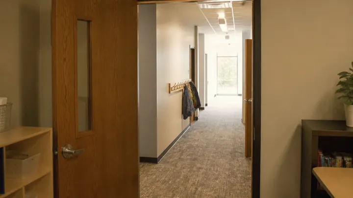 A church classroom doorway with a vision panel, low shelving, and coat hooks in the hallway